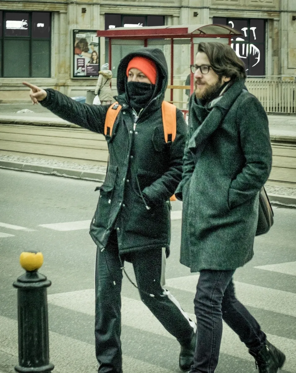 Bundled pedestrian pointing across the street while walking beside a bearded man